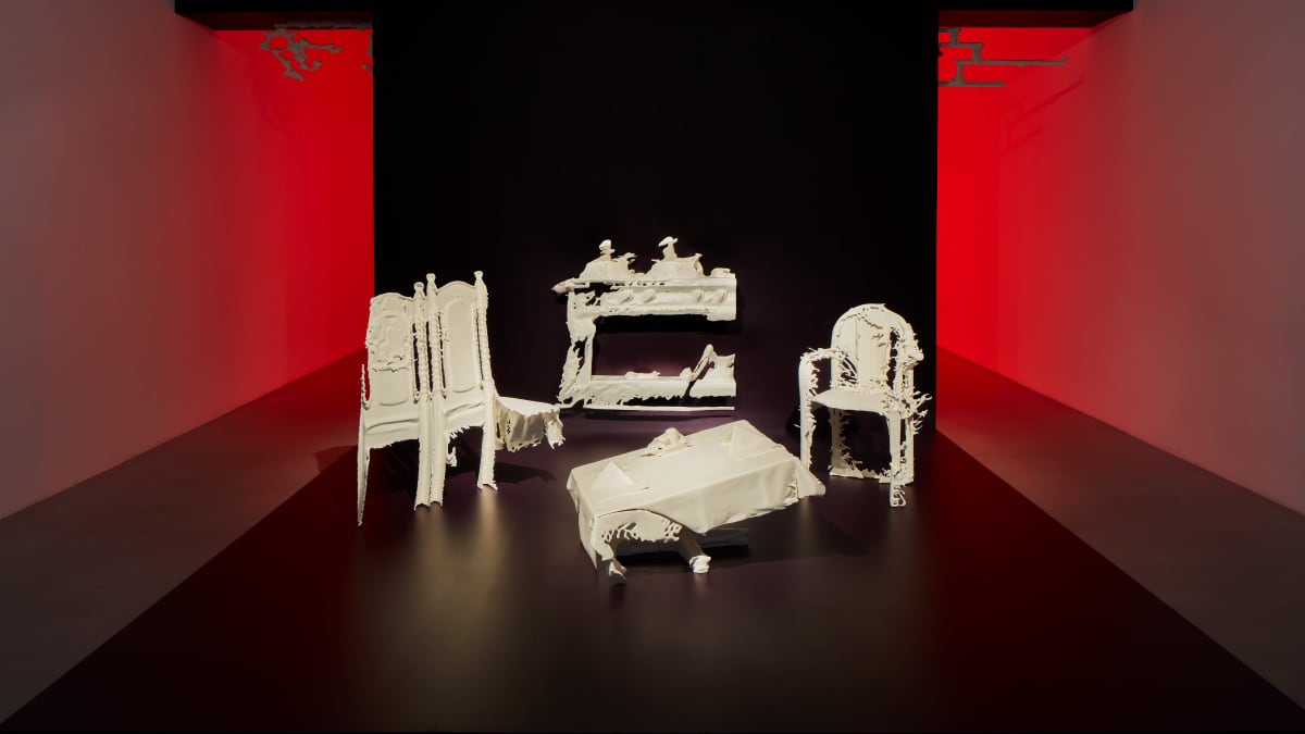 Kuvassa hapertuneelta näyttäviä töitä ja tuoleja punaiseksi valaistussa huoneessa. Kyse on Lap-See Lamin taideteoksesta Phantom Banquet (2020).