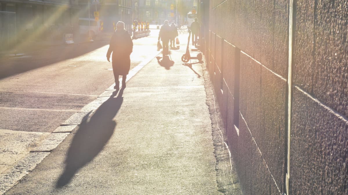 Ihmiset kävelevät kadulla aurinkoa vasten. 