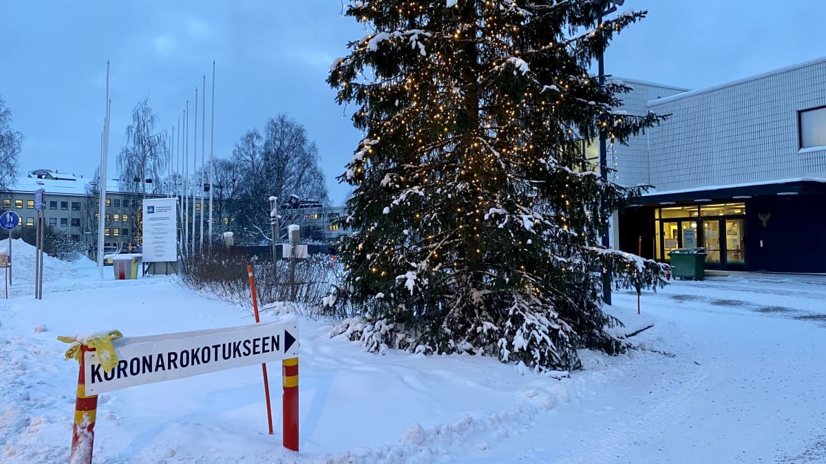 Joulukuusi, jonka taustalla Rovaniemen kaupungin rokotuspiste. Edustalla kyltti, jossa lukee Koronarokotukseen.
