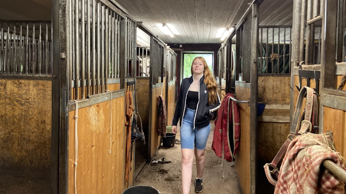 Kuvassa nuori 18-vuotias Silja Lehtonen kävelee hevostallin käytävällä. 