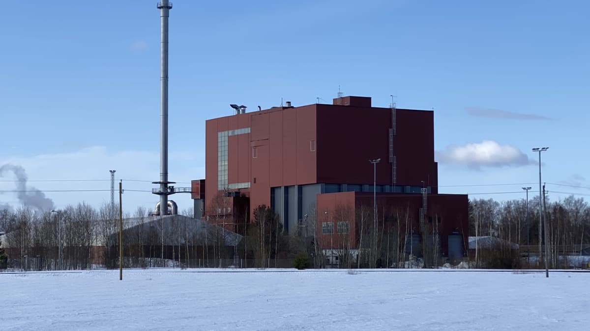 Kuvassa näkyy iso punertava voimalaitos, joka sijoittuu peltomaisemaan.