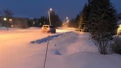 Auto porhaltaa lumisella tiellä katuvalojen loisteessa.