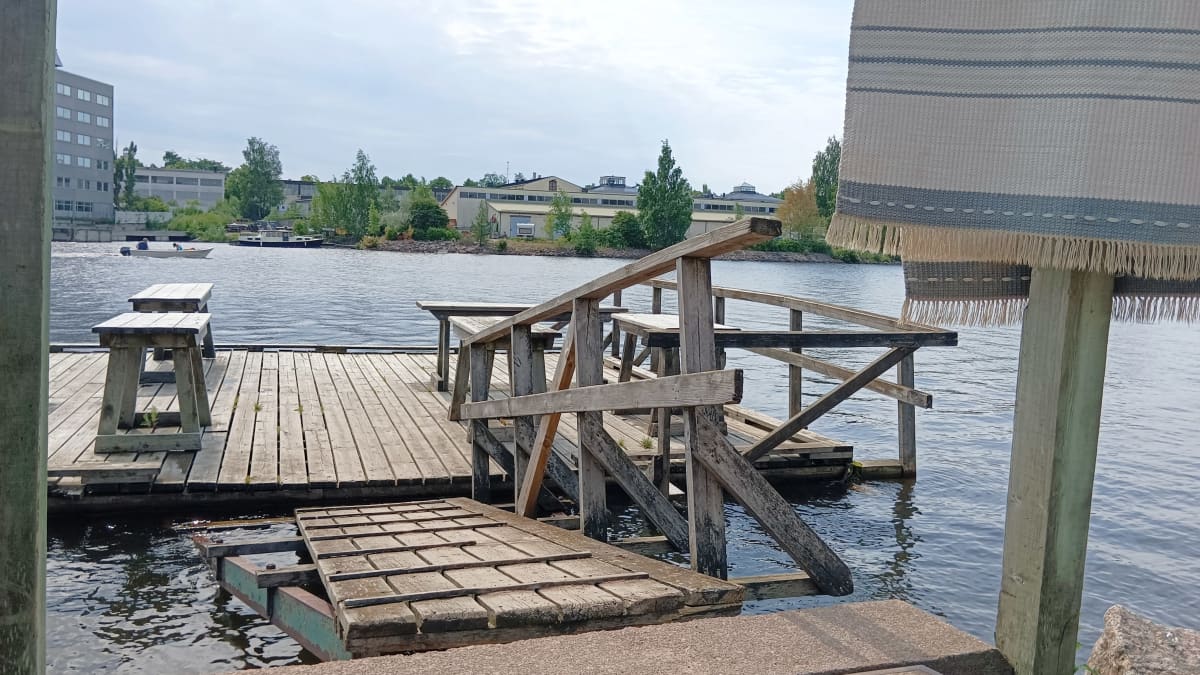 Puinen matonpesulaituri meren rannalla, edustalla roikkuu matto.