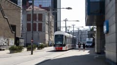 Punavalkoinen raitiovaunu kulkee kadulla, jonka varrella on sekä vanhoja tiilirakennuksia, että uusia lasipintaisia liikehuoneistoja. 