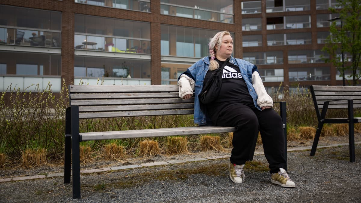 Evaleena Vuorenmaa istumassa penkillä kerrostalojen edustalla.