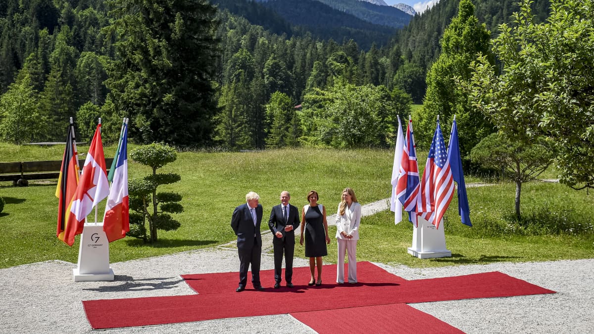 Valtion johtajia kumppaneineen seisoo punaisella matolla vuoristoisessa maisemassa.