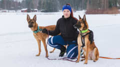Koirahiihdon aktiiviharrastaja Jasmine Dietz kyykistyneenä maassa kahden belgianpaimenkoira malinoisin, Fougan (vasemmalla) ja Vinkan (oikealla) kanssa. Vanhempi koira Vinka istuu omistajansa vieressä, nuorempi pentukoira Fouga seisoo omistajansa toisella puolella. 