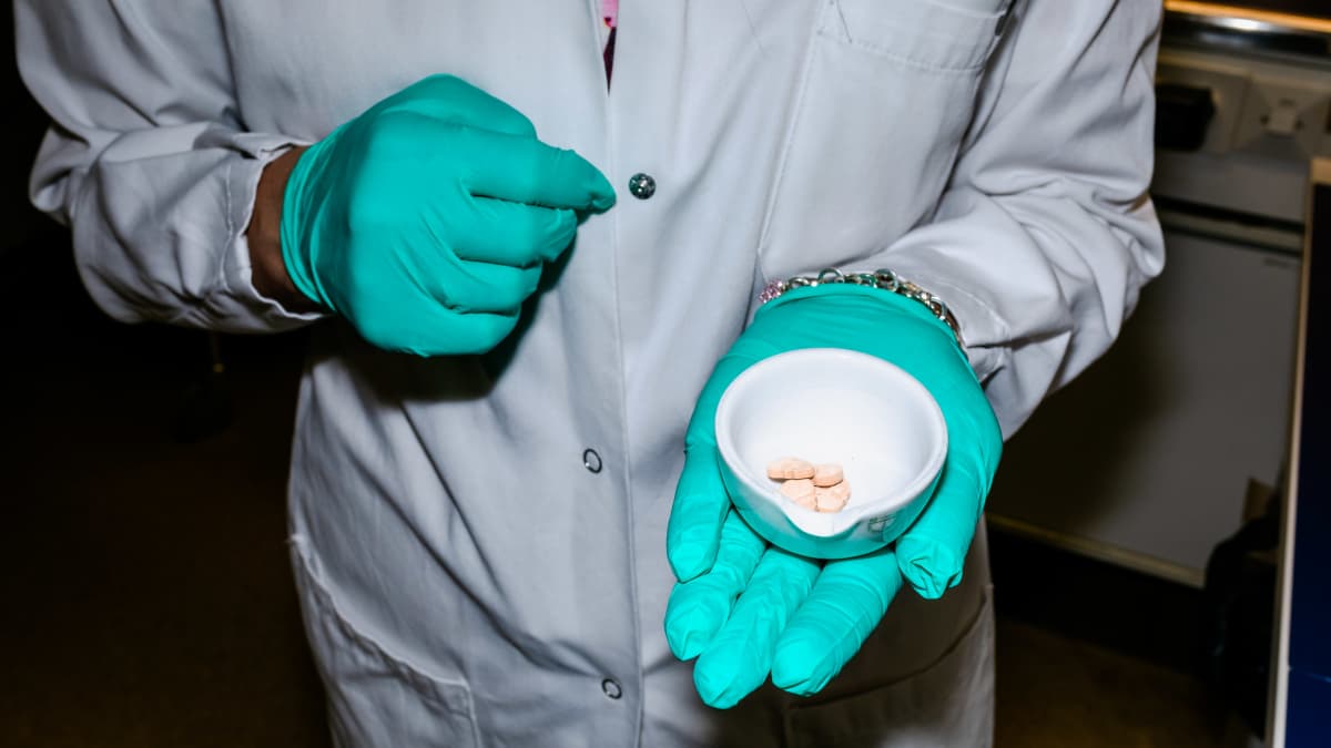 Laboratoriotyöntekijä pitää kädessään pientä kulhoa jossa on ekstaasipillereitä.