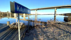 Kalkkisen kylän kyltti Kymijoen rannalla kirkkaana kevätaamuna kuvattuna.