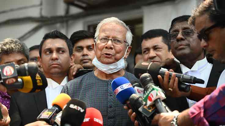 Muhammad Yunus toimittajien ja mikrofonien ympäröimänä.