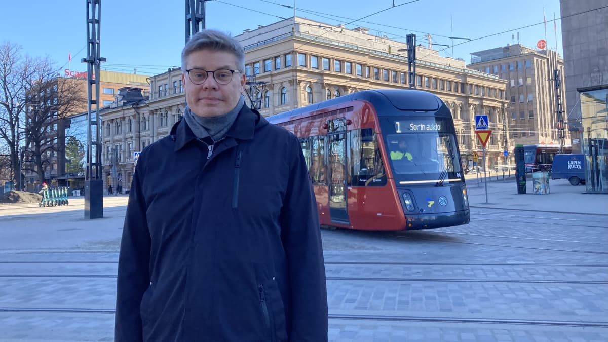 Tampereen Raitiotie Oy:n kehityspäällikkö Ville-Mikael Tuominen seisoo Koskipuistossa, ja 1-linja ratikka kurvaa hänen takanaan Hämenkadulta Hatanpään valtatielle.