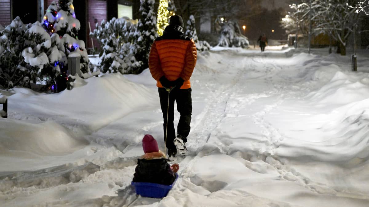 Henkilö vetää lasta pulkassa lumisessa maisemassa.