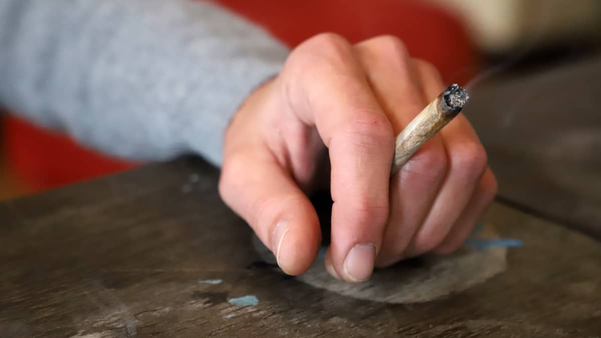 Hand resting on a table, holding a cannabis cigarette.