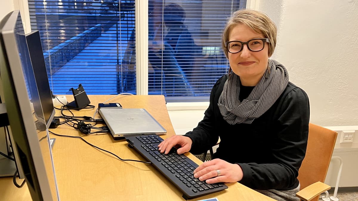 Hymyilevä Iina Ojala istuu työpöydän äärellä ja katsoo kameraan.
