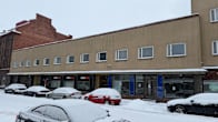 Rakennus taustalla ja lumisia autoja tienvarressa rakennuksen edustalla.