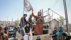 Talibaner sitter på ett bilflak och håller upp en flagga.