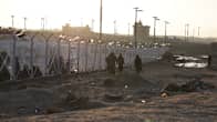 A barbed wire fence with people patrolling in a sandy landscape. 