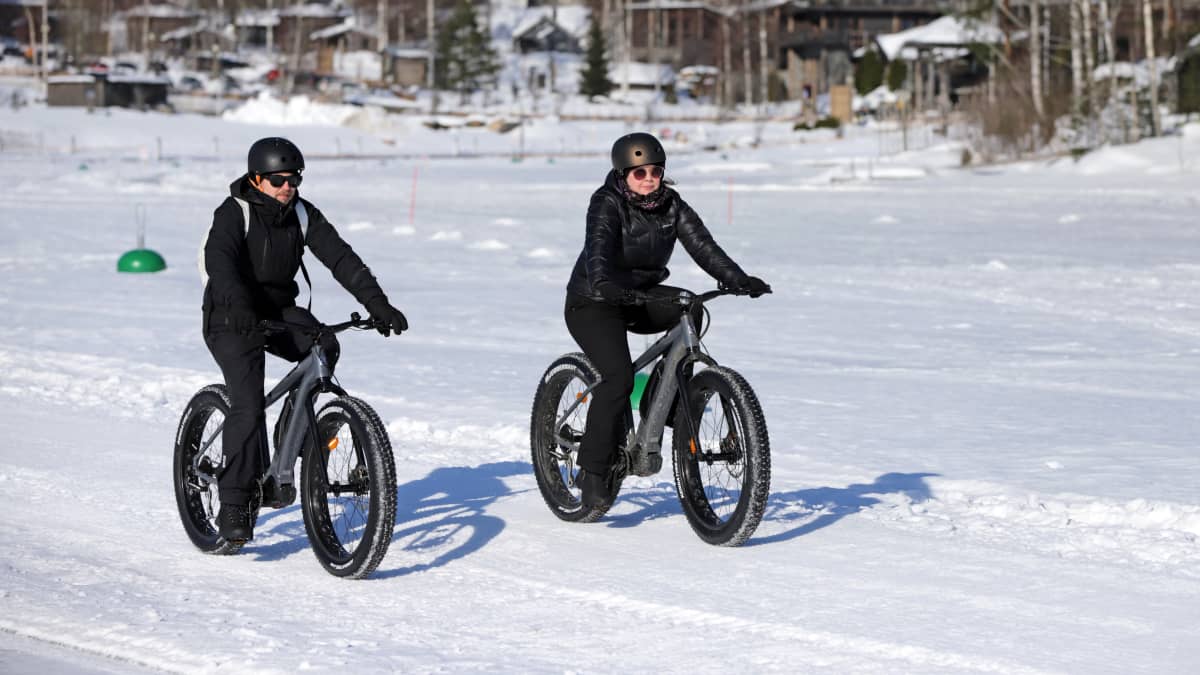Kaksi talvipyöräilijää järven jäällä. Taustalla hotelli Järvisydän.