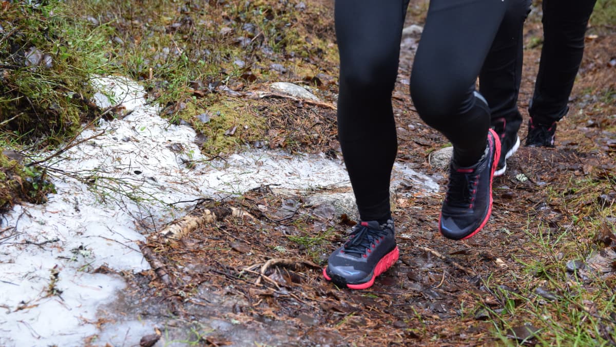 Närbild av fötter med gymnastikskor som pringer på en skogsstig med lite snö på.