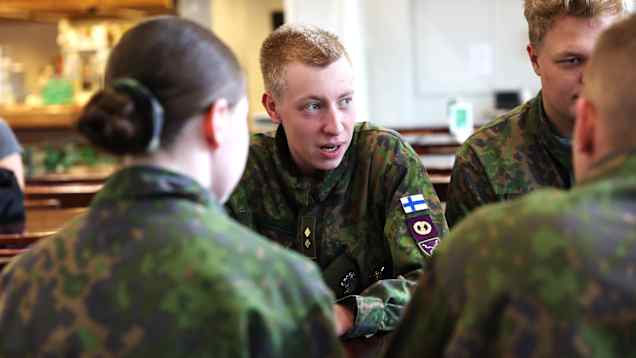 Fyra personer i militäruniform sitter vid ett bord inomhus.