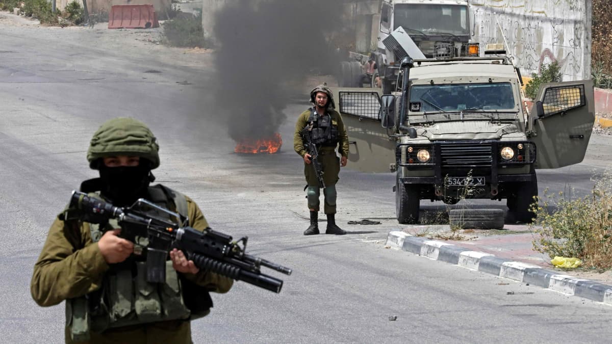 Israelilaisia sotilaita vahtii mielenosoittajia kadulla.