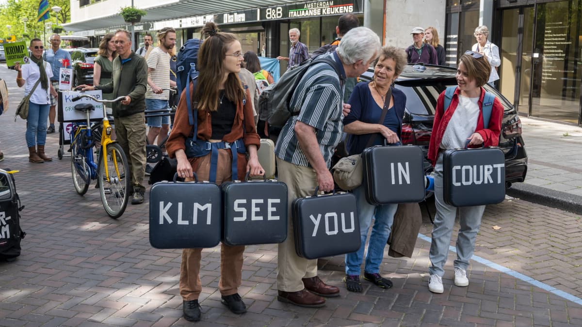 Ihmiset kantavat matkalaukkuja, joissa lukee KLM SEE YOU IN COURT.