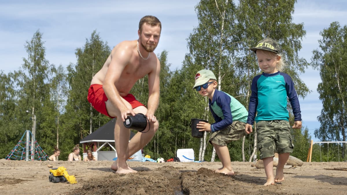 Isä ja pojat leikkivät vedellä Kemin Mansikkanokan uimarannalla. 