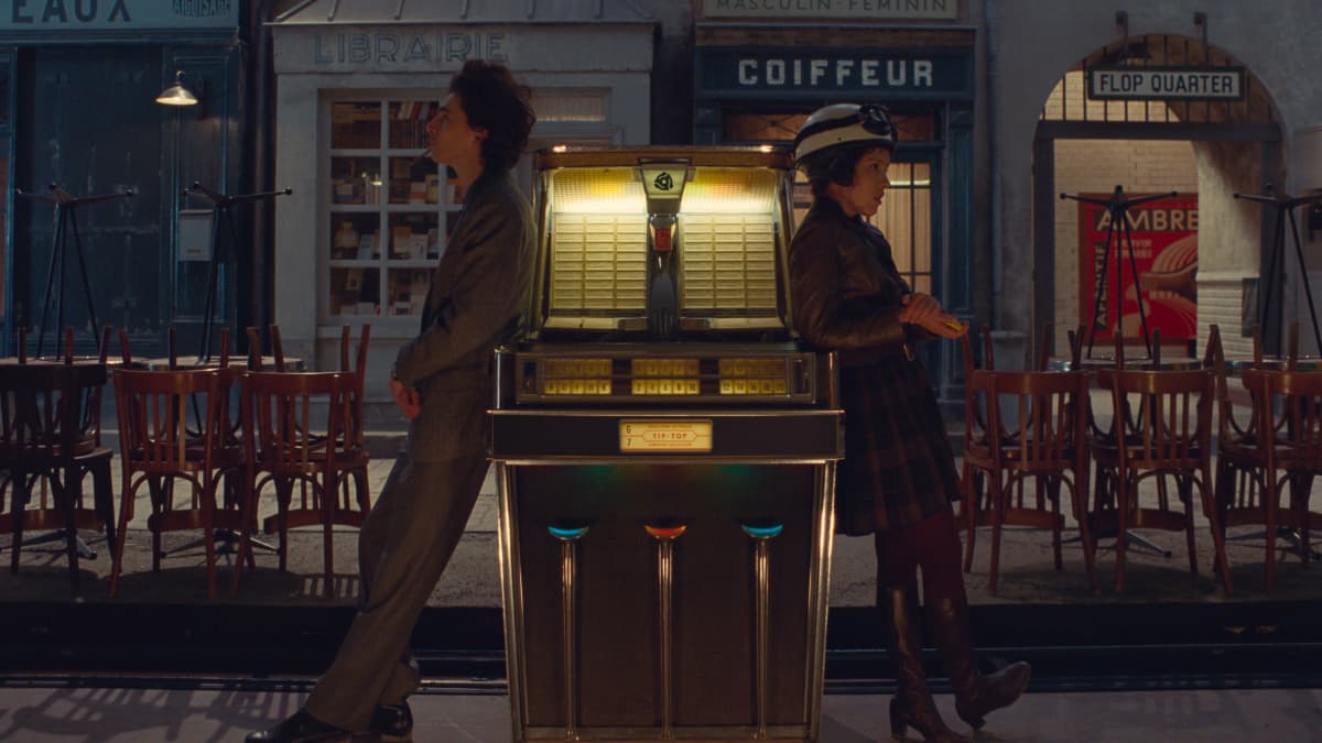 Nainen ja mies seisovat levyautomaatin vieressä kadulla ranskalaiskaupungissa elokuvan pressikuvassa.