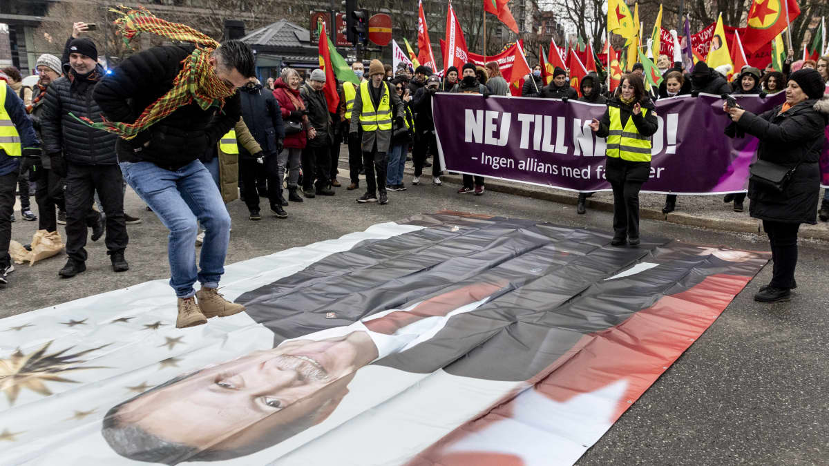 Mielenosoittaja hyppää Turkin presidenttiä kuvaavan bannerin yli Turkin presidenttiä Recep Tayyip Erdogania ja Ruotsin Nato-pyrkimystä vastaan ​​järjestetyn mielenosoituksen aikana Tukholmassa.