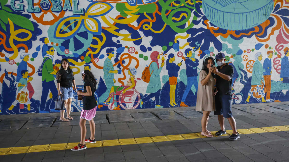 Perhe seisoskelee värikkään seinämuraalin edessä Indonesian Jakartassa 4. joulukuuta 2022.