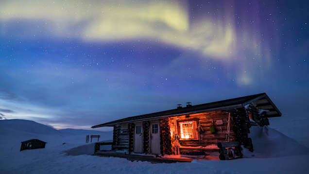 Photo shows a cabin with aurora in the background.