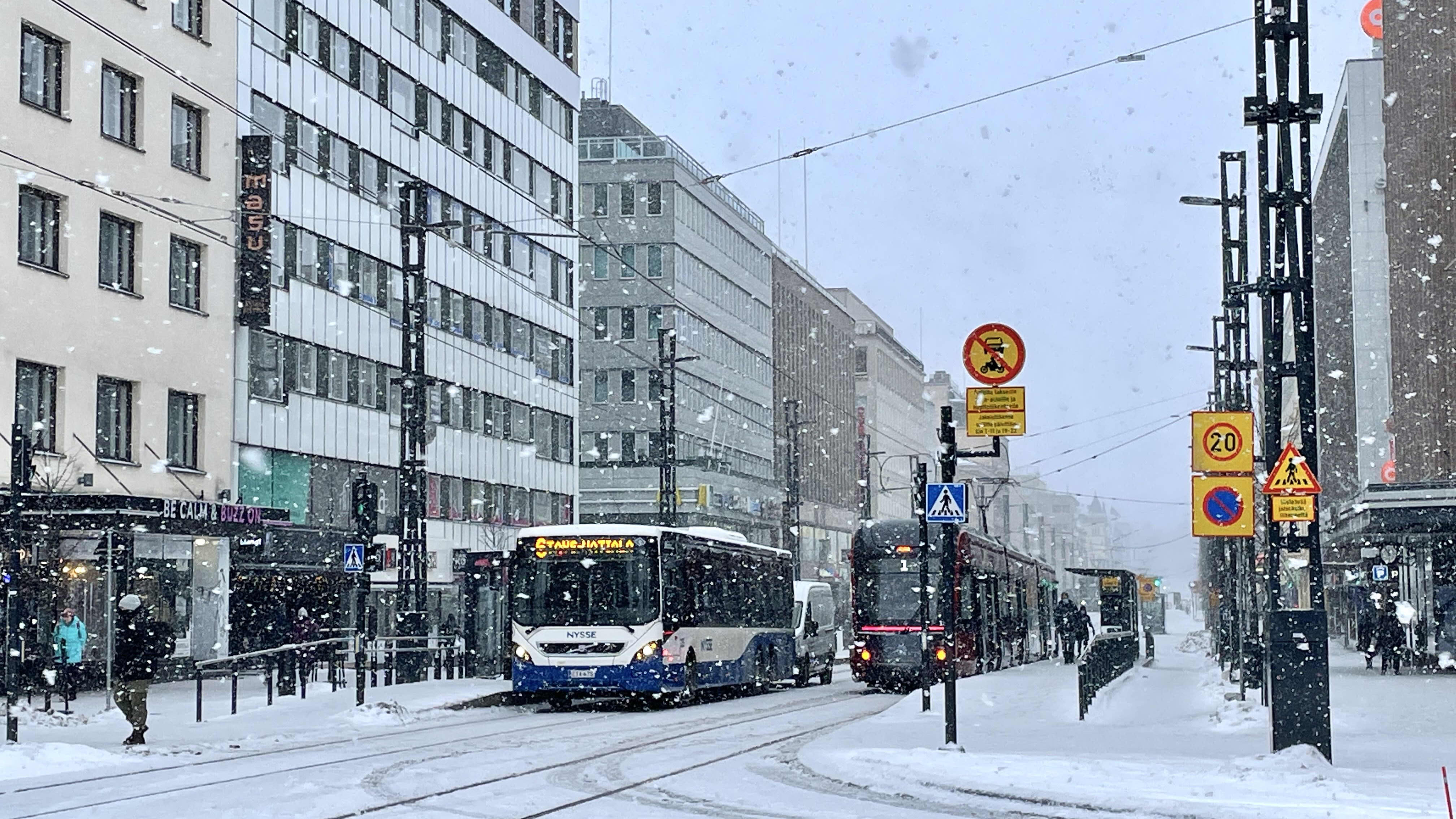 Bussi ja raitiotievaunu seisovat liikennevaloissa lumisateisella Tampereen Hämeenkadulla.