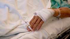 Photo shows the hand of a patient as they lie in a hospital bed.
