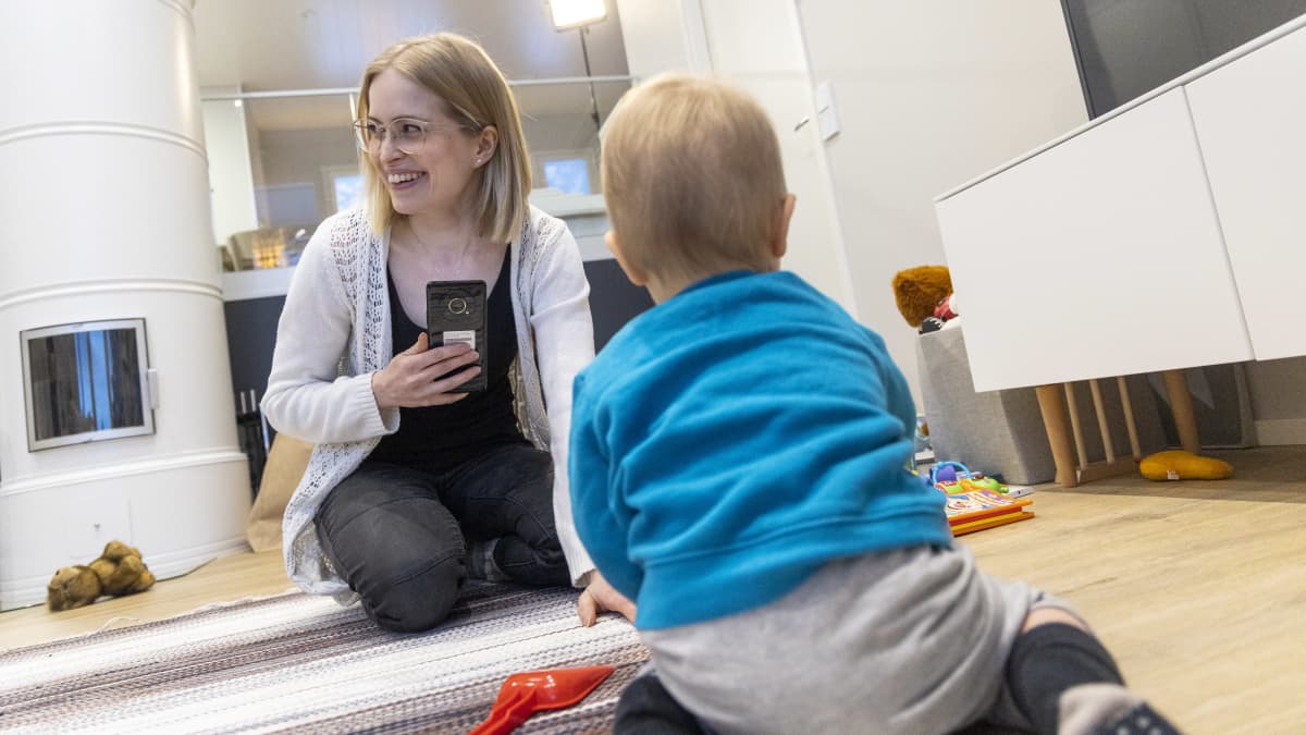 Jenna Ahonen istuu lattialla yhdessä lapsensa kanssa joka leikkii leluilla.