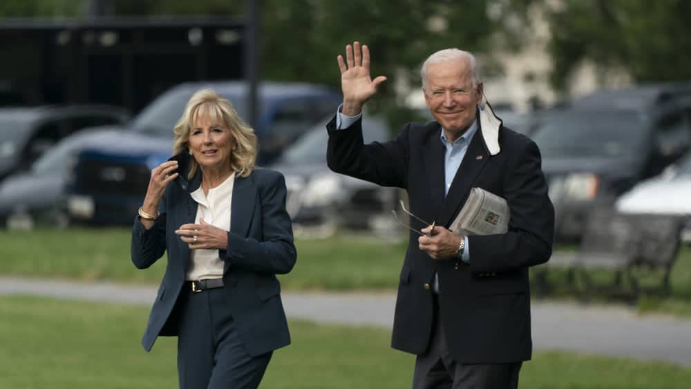 Joe ja Jill Biden ulkona maskit puoliksi kasvoillaan, Joe Biden huiskuttaa kameralle. 