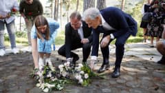 Kolme henkilöä asettelee kukkia maahan muistotilaisuudessa.