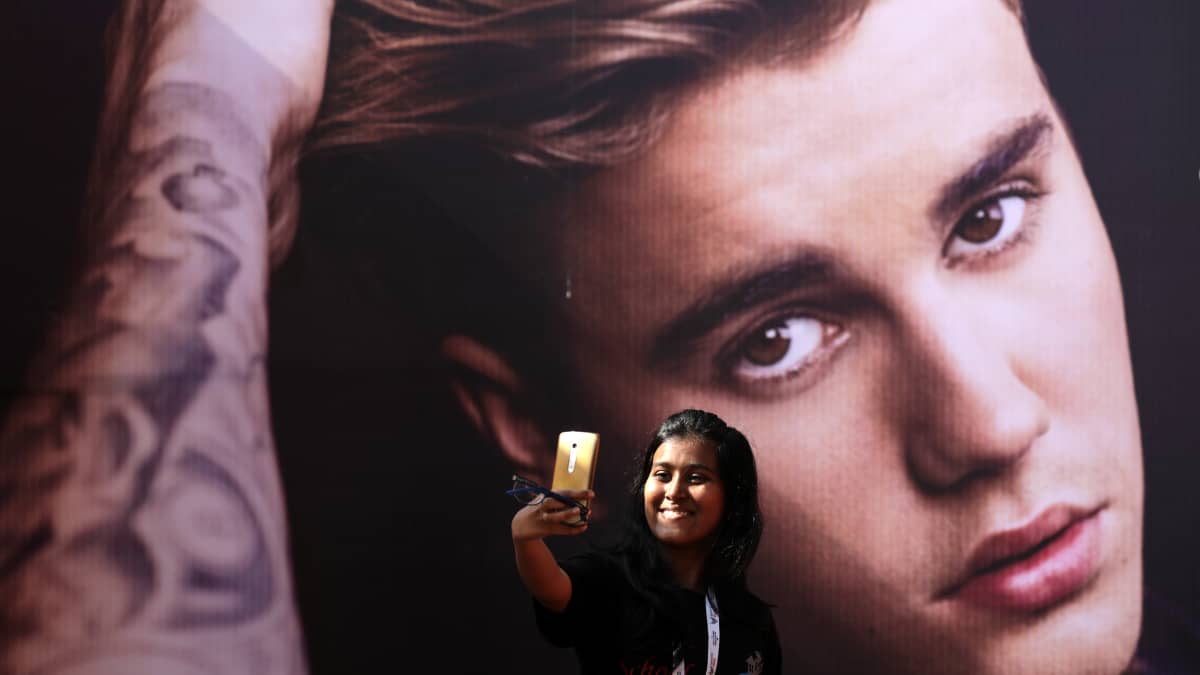 Nainen ottaa selfietä Justin Bieberin jättikokoista kuvaa vasten.