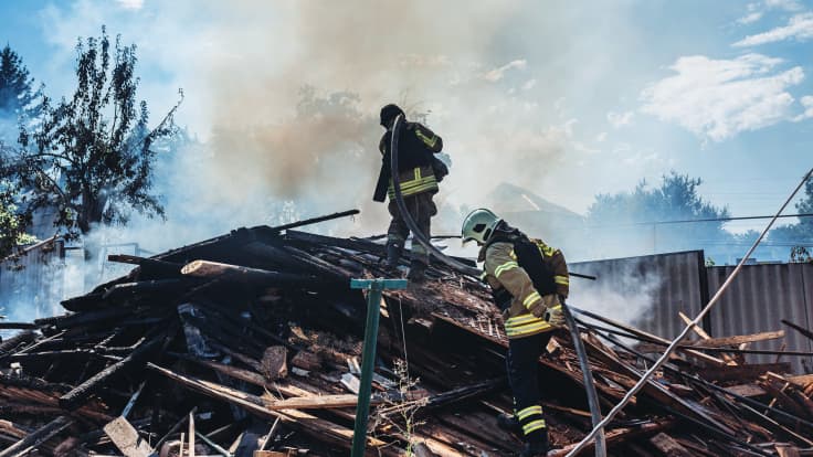 Palopelastajat kipuavat savuavien raunioiden päälle sammuttamaan paloa.