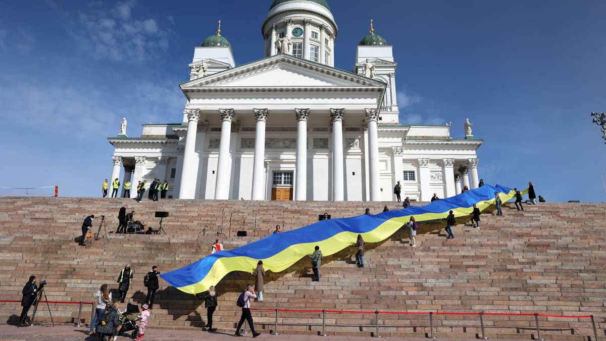 Ihmiset kantavat valtavan kokoista Ukrainan lippua Tuomiokirkon portailla.