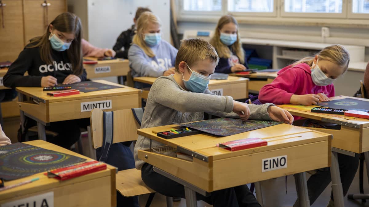 oppilaat istuvat pulpeteissaan maskit kasvoilla ja keskittyvät piirtämään vahaliiduilla