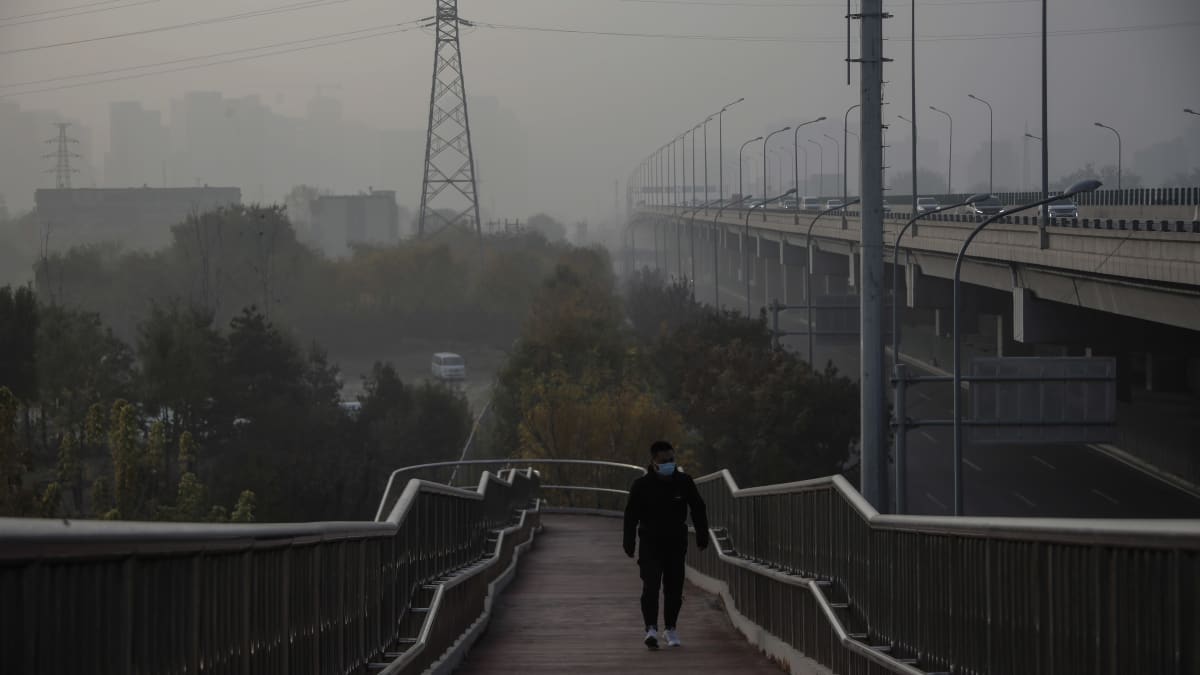 Saastesumu peitti taivaanrannan Pekingissä. Kävelijä kulki kaupungissa siltaa pitkin. 