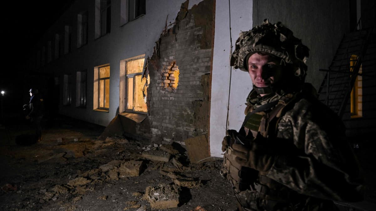 Sotilas seisoo vartiossa vaurioituneen talon edustalla.