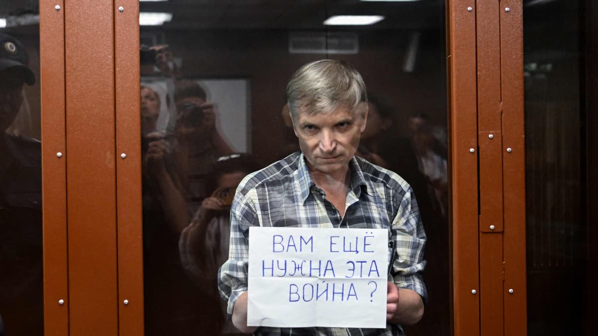 Gorinov on lasikopissa ja näyttää lappua, jossa lukee venäjäksi "Tarvitsetteko yhä tätä sotaa?".