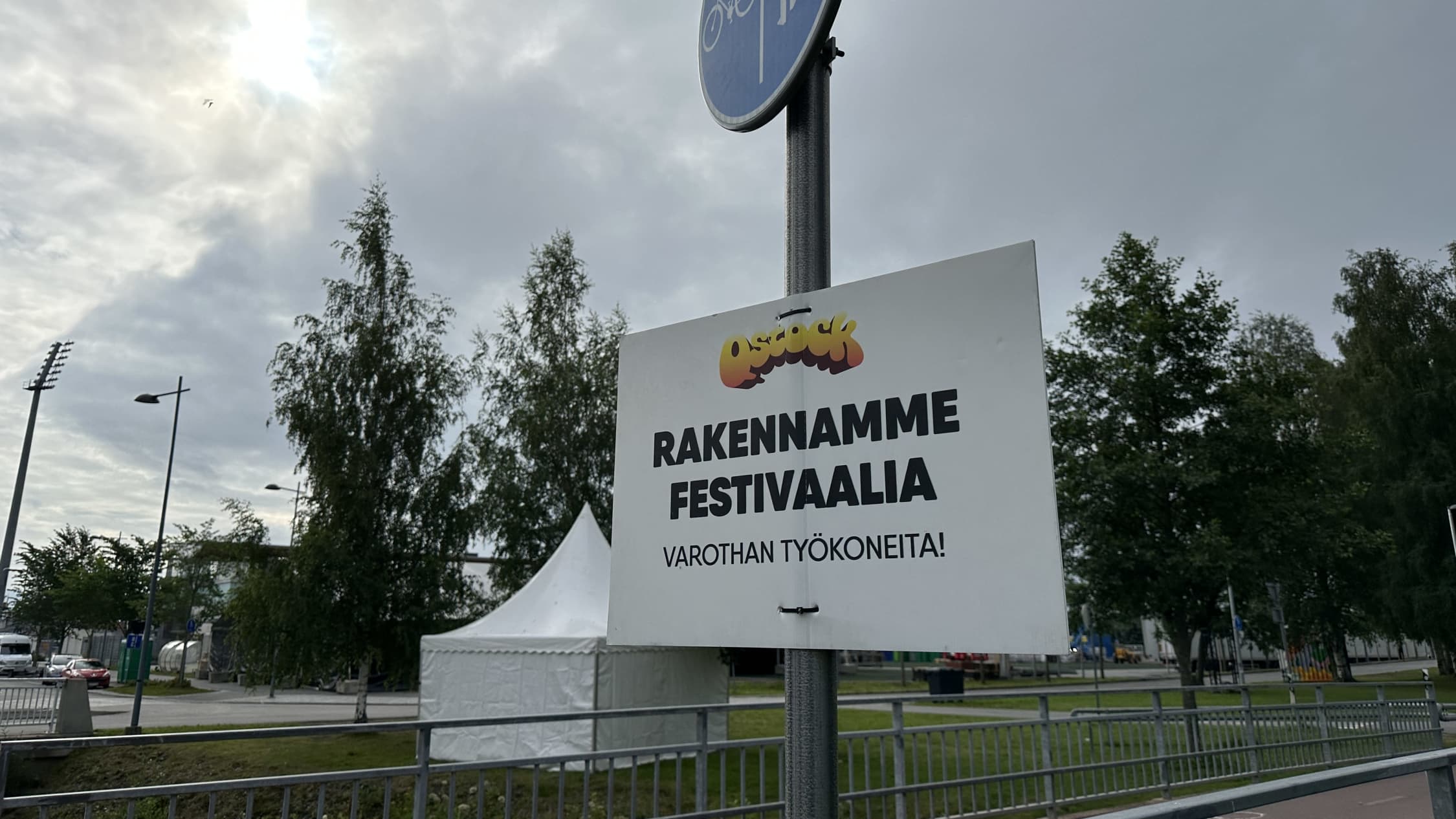 Varoituskyltti, jossa lukee: rakennamme festivaalia, varothan työkoneita. 