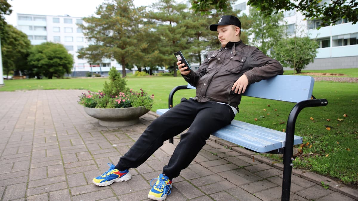Turkulainen Jyrkkälän lähiö. Nuorehko asukas istuu keskipihan penkillä ja selailee puhelintaan. 