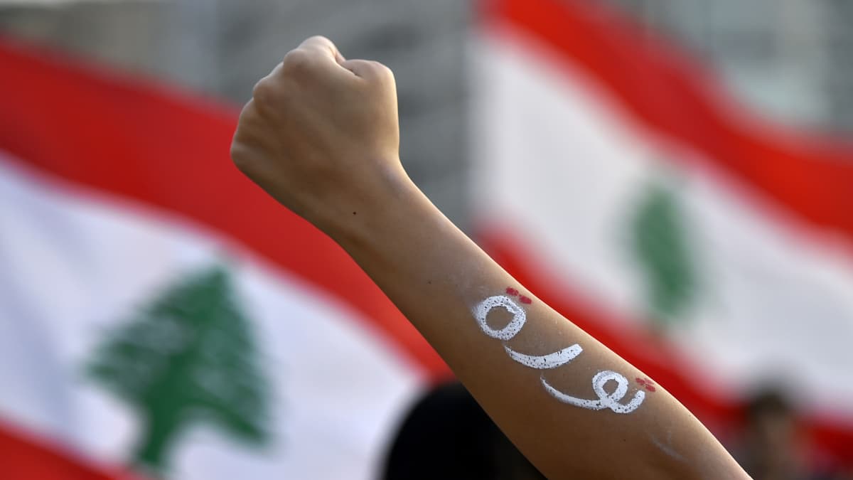Nyrkkiin puristunut käsi. Taustalla Libanonin lippu.