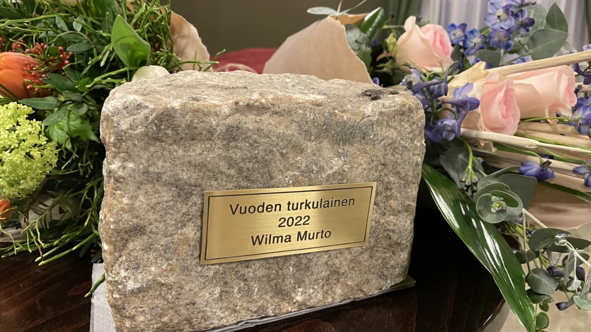 Vuoden turkulainen 2022 Wilma Murto -laatta kiveen kiinnitettynä. Palkinnon vieressä pöydällä kukkasia.