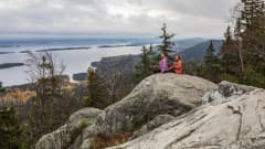 Kaksi naista istuu syksyllä Kolin huipun kallioilla.