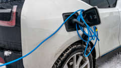 Sähköauton sininen latausjohto vyyhtinä auton latausluukun ympärillä.