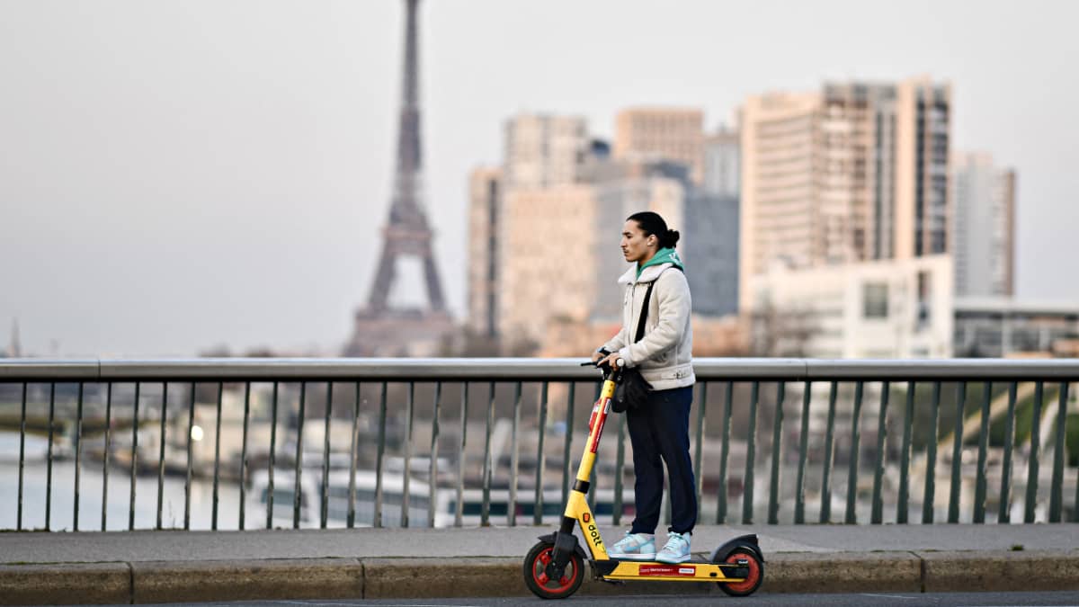 Nuori mies ajelee sähköpotkulaudalla Pariisissa. Sillan takana näkyy Eiffel-torni.